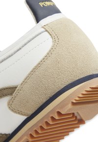 White and beige sneaker with suede and smooth leather, featuring a textured rubber sole and gold branding on the heel.