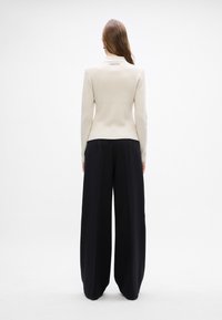 Kremfarget ribbestrikket genser med en tettsittende silhuett, parret med høyt liv sorte vide bukser. Minimalistisk design med logodetalj.