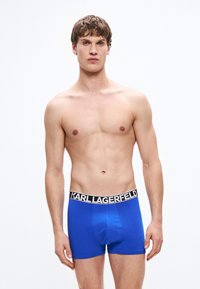 Niebieskie bawełniane bokserki z czarną elastyczną talią z logo "KARL LAGERFELD". Gładka tekstura, dopasowany krój, długość do połowy uda.