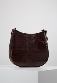 Viininpunainen tekonahkainen käsilaukku krokotiilimallisella pintakuviolla, pyöreä muoto, kullanväriset metalliosat ja yksittäinen säädettävä olkahihna.