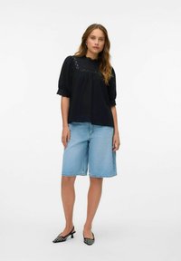 Svart texturerad blus med puffärmar, denimbermudashorts och mönstrade svarta klackar. Blusen har spetsdetaljer vid halsringningen.
