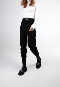 Pantalons noirs taille haute avec des jambes fuselées, associés à un col roulé côtelé blanc et des bottes noires épaisses avec un détail de chaîne métallique brillante.