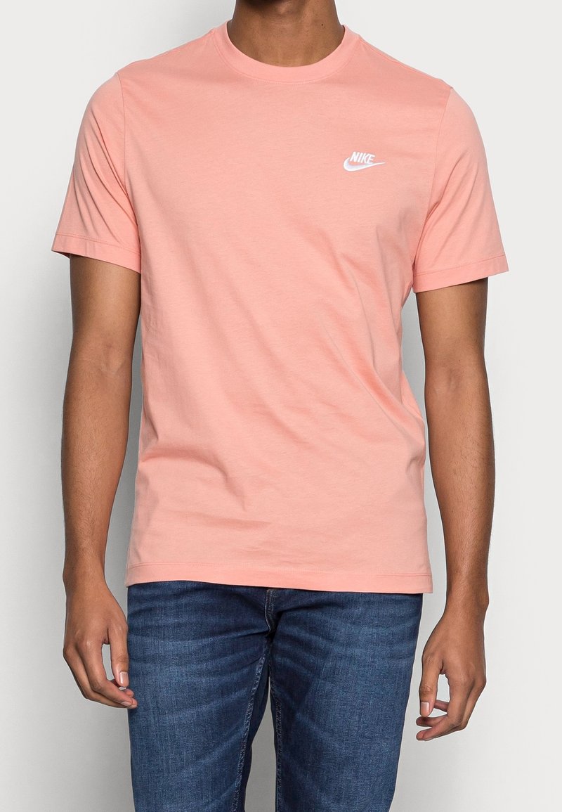 Světle růžové tričko s krátkým rukávem od Nike vyrobené z bavlny, s malým bílým logem na levé hrudi. Hladký povrch, design s kulatým výstřihem.