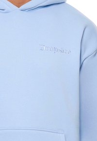 Gaiši zila kapuce, kas izgatavota no mīksta auduma, ar izšūtu "Dropsize" logotipu kontrastējošā tonī. Ietver priekšējo kabatu.