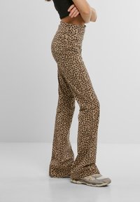 Kalhoty s leopardím potiskem ve střihu do zvonu vyrobené z měkké tkaniny, s vysokým pasem a hladkým povrchem. Barevná paleta zahrnuje hnědé a béžové odstíny.