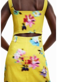 Top corto amarillo floral con escote cuadrado, que presenta un patrón de flores en tonos rosa, azul y púrpura, acentuado por un diseño de espalda abierta.