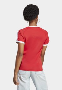 Czerwona koszulka z krótkim rękawem i białymi akcentami. Posiada okrągły dekolt i rękawy raglanowe. Gładki materiał, dopasowany krój.