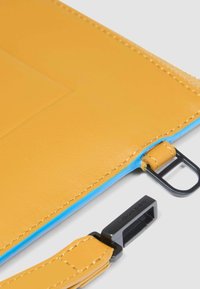 Gele leren laptoptas met een blauwe binnenkant, voorzien van een ritssluiting en zwarte hardwareaccenten. Vloeibare textuur met nauwkeurige stiksels.