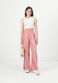 Pantalons wide-leg avec un motif rose et violet vif, fabriqués à partir d'un tissu léger. Assortis à un crop top blanc ajusté et un sac en toile.