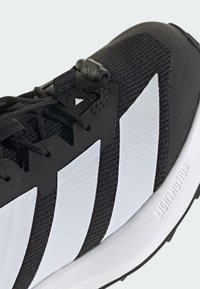 Μαύρο αθλητικό παπούτσι με λευκές ρίγες. Διαθέτει επάνω μέρος από διχτυωτό υλικό, υφή υφάσματος και καουτσούκ σόλα. Ρυθμιζόμενο σύστημα κορδονιών στο μπροστινό μέρος.