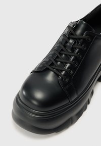 Black leather lace-up shoes with a rounded toe, thick sole, and visible stitching. The design features textured accents on the heel.