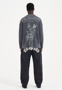 Maglietta grigia a maniche lunghe con texture a coste e un design grafico sulla schiena. Pantaloni neri con la scritta audace "Ed Hardy" sul retro.