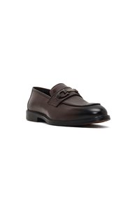Mocassino da uomo in pelle marrone con punta nera, fascetta decorativa e tacco basso, mostrato da un angolo leggero su uno sfondo bianco.