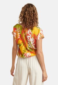 Korte mouwen blouse in felgeel, versierd met tropische patronen in groen, roze en oranje; zachte stof met een ontspannen pasvorm.