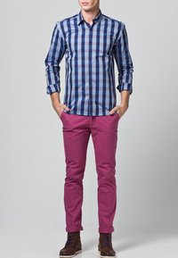 Niebiesko-biała koszula w kratę na guziki, zestawiona z dopasowanymi, magentowymi spodniami. Modelka nosi brązowe buty na sznurowadła.