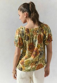 Blusa floral en tejido ligero, con un escote fruncido, mangas cortas abullonadas y vibrantes patrones de girasoles en amarillo, naranja y verde.