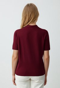 Bordowa polo z krótkim rękawem o miękkiej strukturze, z ribbowanym kołnierzykiem i mankietami oraz prostym dołem. Minimalistyczny design.