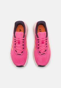 Zapatos deportivos de un vibrante color rosa, con una parte superior de malla transpirable, detalles en negro, plantillas naranjas y una suela blanca moteada.