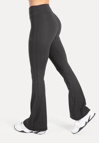 Svarta utsvängda leggings av stretchigt tyg med hög midja och kontrasterande sömmar. Kombinerade med vita sportskor.