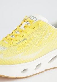 Bottine de sport jaune avec une tige en maille présentant un motif en grille, des accents blancs, des lacets jaunes et une semelle blanche rembourrée avec des découpes.
