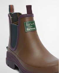 Bota Chelsea de borracha castanha com detalhes em roxo, painéis laterais elásticos e forro de padrão xadrez. Apresenta uma etiqueta de marca no lado exterior.