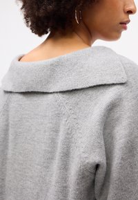 Svijetlosiva oversized dukserica s širokim rebrastim ovratnikom i suptilnom teksturom, s raglan rukavima i čistim detaljima šivanja.