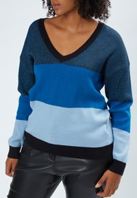 Maglione a righe blu e nere con scollatura a V profonda, realizzato in morbido materiale lavorato a maglia, dotato di diverse tonalità di blu e neri in rilievo.