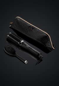 Haarstylingshulpmiddelen omvatten een zwarte ovale borstel, een ronde stylingborstel met een gestructureerde handgreep en een zwarte opbergtas met slangenpatroon en gouden accenten.