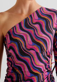 Haut asymétrique avec un motif ondulé multicolore de rose, bleu et orange sur fond noir, avec un détail froncé sur un côté.