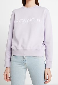 Sudadera de color púrpura claro hecha de mezcla de algodón, con cuello redondo y puños acanalados, con el logo "Calvin Klein" en blanco en el pecho.