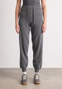 Grå strikkede joggebukser har snor i livet, elastiske mansjetter og en avslappet passform. Kombinert med grå joggesko og hvite sokker.