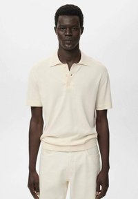 Vaaleanbeige lyhythihainen polo-paita, jossa on ribbireunus kauluksessa ja hihoissa, sekä kolme nappia sisältävä napitus ja pehmeä rakenne.