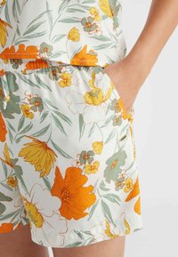 Bloemenkorte broek van een lichtgewicht stof met oranje, gele en groene bloemen op een witte achtergrond, voorzien van een elastische tailleband en zijzakken.