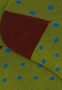 Grüner, texturierter Stoffsocke mit braunem Fersenbereich und blauen Punkten, die ein Strickmuster und kontrastierende Farbabschnitte zeigt.