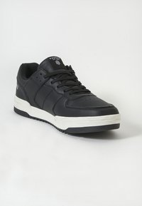 Adidași negri cu un superior din piele netedă, talpă albă și talpă exterioară din cauciuc texturat. Include șireturi și detalii perforate pe vârf.