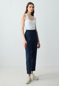 Weißes, geripptes Tanktop kombiniert mit navyblauen, dehnbarem Bund Hosen. Das Modell trägt cremefarbene Sneakers. Minimalistisches Design und lässige Passform.