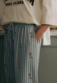 Světle modré pruhované pyžamové kalhoty s volným střihem, se zobrazením malých psích ilustrací. Vyrobené z měkké tkaniny s elastickým pasem.