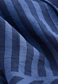 Tissu bleu avec des rayures verticales alternées foncées et claires, légèrement froissé et se chevauchant, avec des détails de texture visibles.