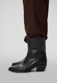 Bottines en cuir noir avec talons bas portées avec un pantalon brun foncé.