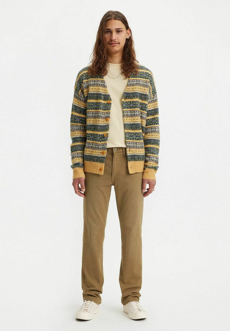 Gebreide cardigan met groene, gele en blauwe strepen, met houten knopen; gecombineerd met een crèmekleurig t-shirt en kaki broek.