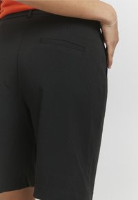 Schwarze, maßgeschneiderte Shorts mit glatter Textur, ausgestattet mit einer einzigen Gesäßtasche und mittelhohem Bund. Klassisches Design, geeignet für verschiedene Anlässe.