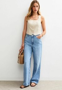 Beige gestreepte crop top met knopen aan de voorkant, gecombineerd met lichtblauwe wijde jeans. Geaccessorieerd met een geweven handtas en sandalen.