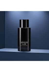 Flacon noir d'Armani Code Eau de Toilette avec texte argenté-blanc, posé sur une étagère bleue contre un fond bleu foncé.
