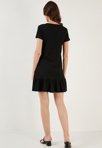 Black short-sleeve dress with a ruffled hem, made from textured fabric. The back has a simple neckline and is fitted at the waist.