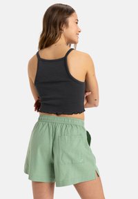Zwart geribbeld crop top met golfkante, gecombineerd met groene linnen shorts met een elastische tailleband en een achterzak.