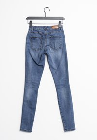 Jeans ajustados de color azul con un leve desgaste, hechos de mezclilla. Cuentan con bolsillos traseros y un parche de cuero marrón cosido en la cinturilla.