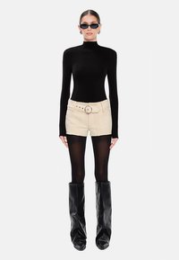 Sort langærmet rullekrave, beige shorts med en rund bæltespænde, sorte strømpebukser og høje sorte støvler med en slasket tekstur.