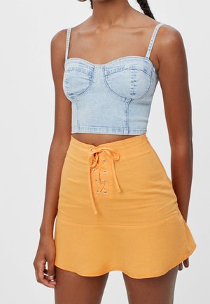 Kvinde iført lyseblå denim croptop med spaghetti-stropper og orange mininederdel med snøredetalje foran i taljen.