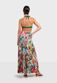 Twee-delige outfit: groene haltertop met een klapsluiting op de rug, gecombineerd met een lange, kleurrijke maxi-jurk met bloemenpatronen en levendige bloemenprints.