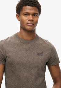 Grå kortærmet t-shirt lavet af blødt stof med rund halsudskæring. Har et lille mørkeblå logo på venstre brystområde.